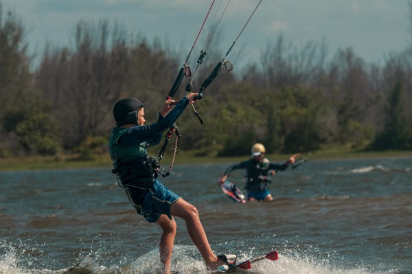 A student riding across the flat water of Cauípe lagoon with Wendell watching behind