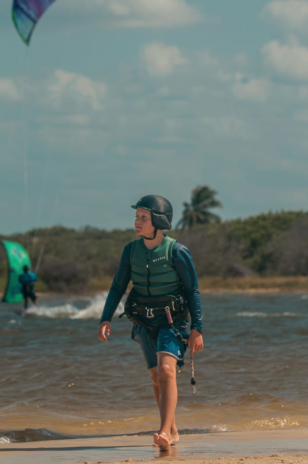 A young student in helmet and vest walking out of the lagoon onto the sand